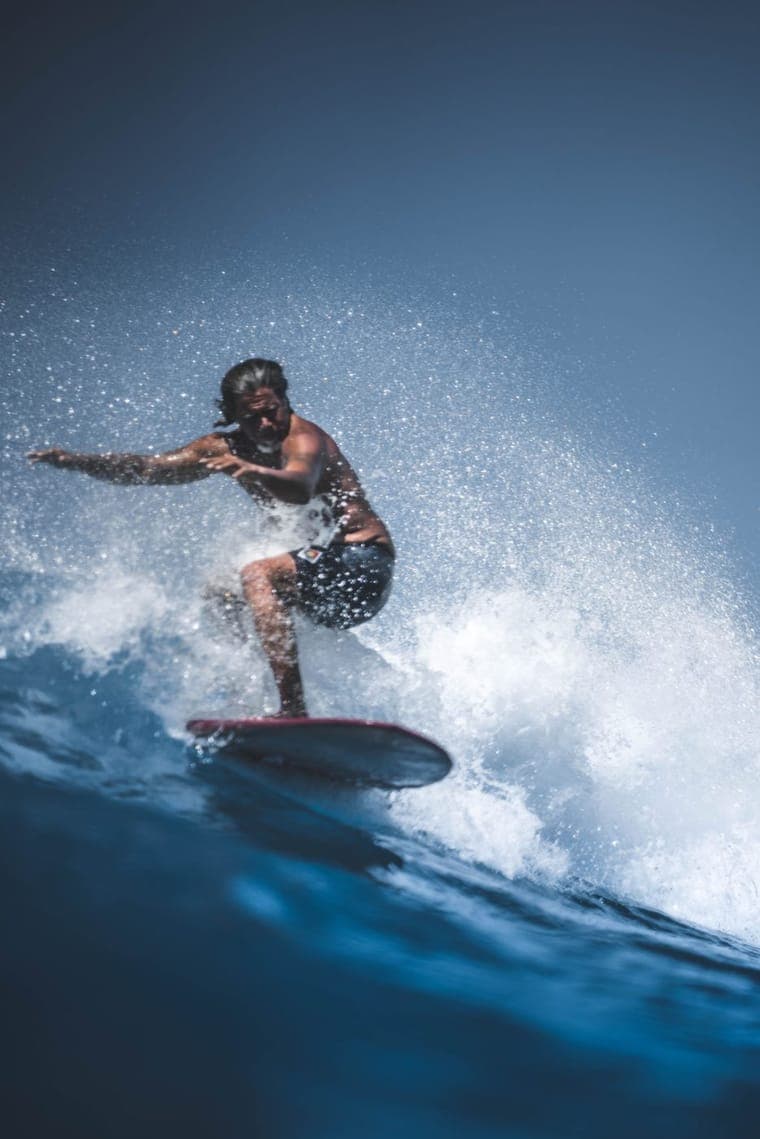 Ein Surfer fährt in geduckter Haltung durch die Gischt einer brechenden Welle