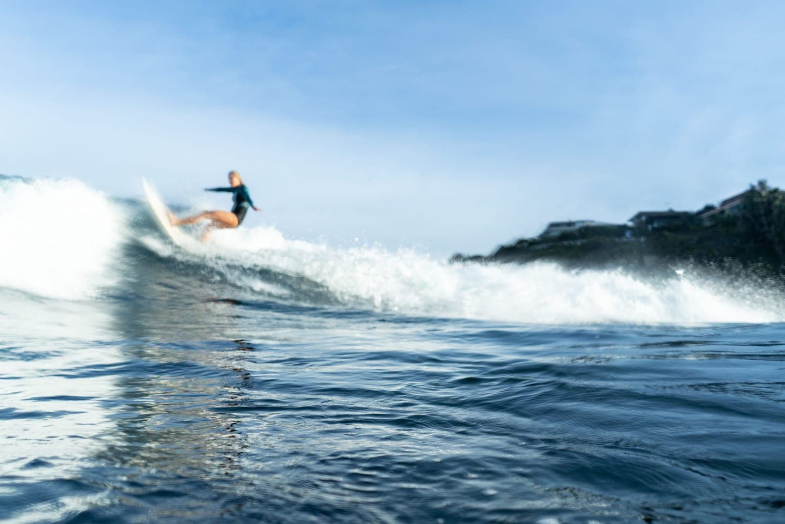 Surferin fährt mit ausgestreckten Armen eine Welle entlang, Bewegungsunschärfe im Vordergrund