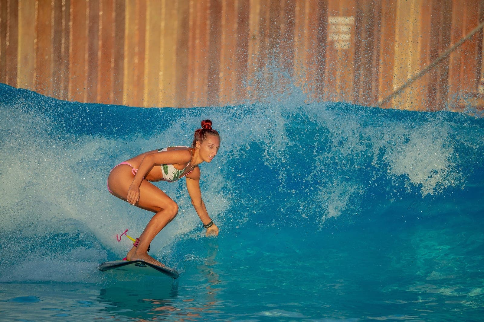Surferin in geduckter Haltung auf dem Brett in einem Wellenbecken, umgeben von aufspritzender Gischt